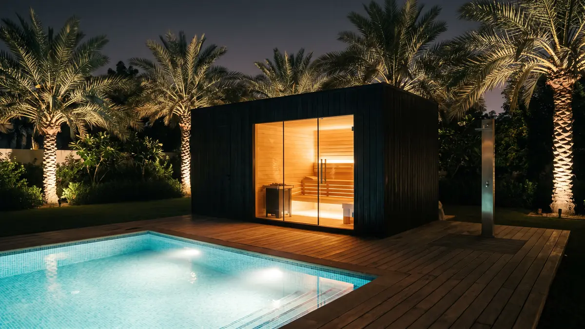 Outdoor sauna pavilion with glass front beside an illuminated pool in a Dubai villa garden